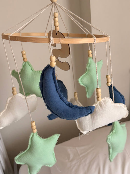 Close-up of a blue crescent moon, mint green stars and white fabric clouds on a personalized baby mobile