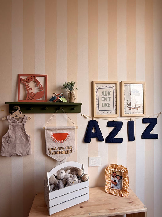 Personalized navy denim letter garland spelling Aziz, displayed on a nursery wall with wooden shelves, framed artwork and children’s room accessories.