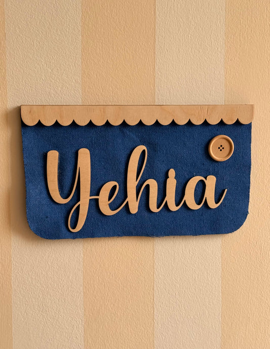 Personalized royal blue textured fabric name banner with natural wooden lettering, a scalloped wooden top trim, and a wooden button detail, ideal for a kids’ room or nursery.