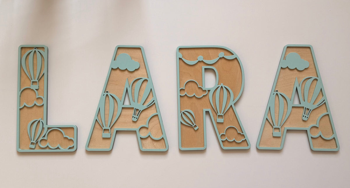 Personalized wooden name wall decor in a mint green and natural wood finish, featuring decorative hot air balloons and clouds integrated into the letters.