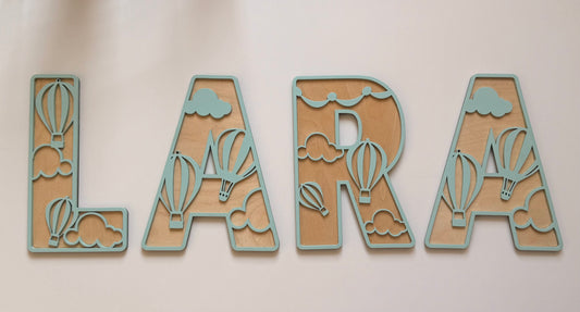 Personalized wooden name wall decor in a mint green and natural wood finish, featuring decorative hot air balloons and clouds integrated into the letters.