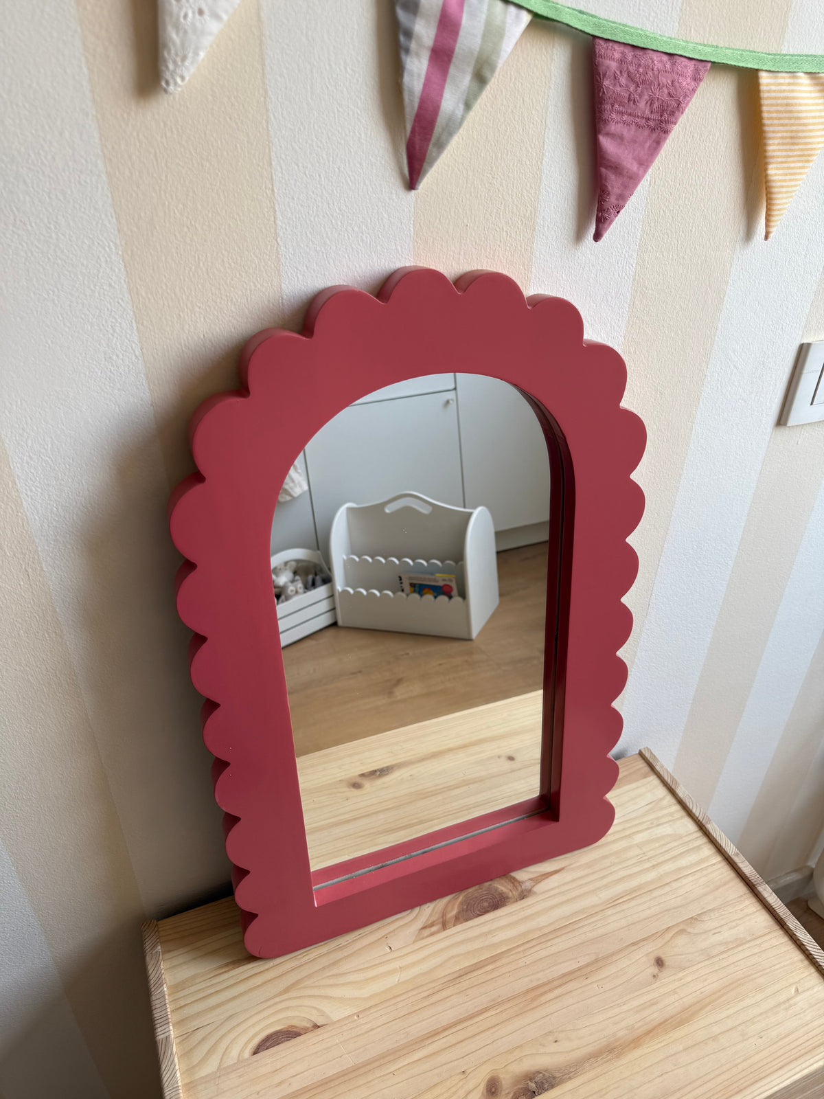 Dusty rose scalloped arch mirror styled on a wooden dresser in a cozy kids’ room with colorful fabric bunting.