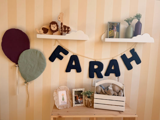 Navy denim personalized name garland spelling Farah, styled with colorful balloon cushions, cloud shelves and wooden nursery accessories.